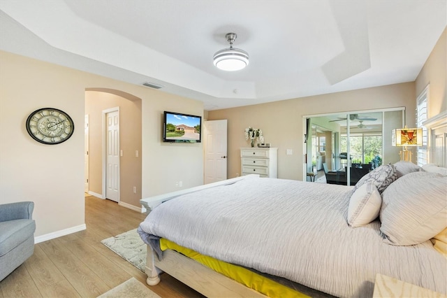 bedroom with light hardwood / wood-style flooring, access to exterior, and a tray ceiling