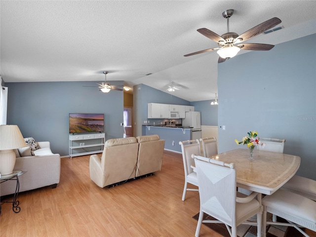 dining room with lofted ceiling, ceiling fan, light wood-type flooring, and a textured ceiling