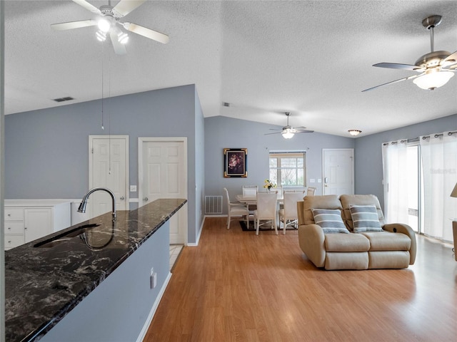 living room with a textured ceiling, light wood-type flooring, sink, and vaulted ceiling