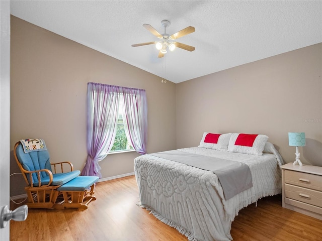 bedroom with a textured ceiling, vaulted ceiling, light hardwood / wood-style flooring, and ceiling fan