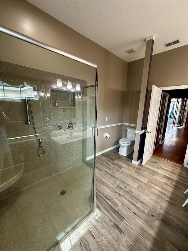 bathroom with a textured ceiling, toilet, hardwood / wood-style floors, and an enclosed shower