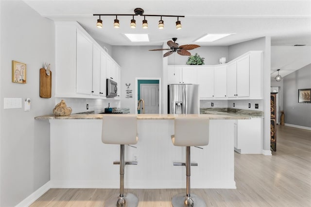 kitchen featuring kitchen peninsula, appliances with stainless steel finishes, a skylight, and white cabinets