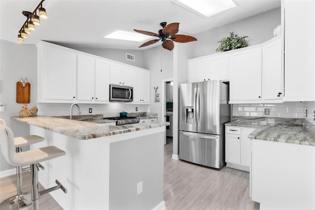 kitchen featuring white cabinetry, stainless steel appliances, tasteful backsplash, kitchen peninsula, and a kitchen bar