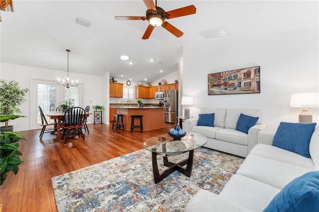 living room with sink, vaulted ceiling, hardwood / wood-style flooring, and ceiling fan with notable chandelier