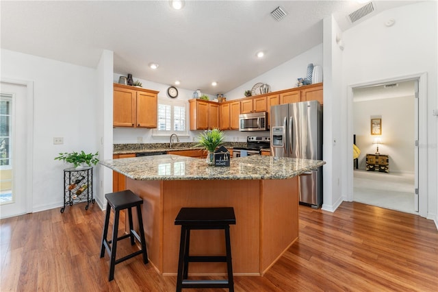 kitchen with stainless steel appliances, lofted ceiling, light hardwood / wood-style floors, and a kitchen island