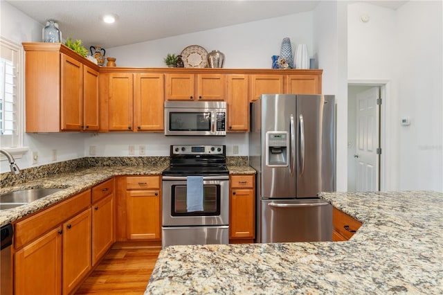 kitchen with light stone counters, stainless steel appliances, light wood-type flooring, sink, and lofted ceiling