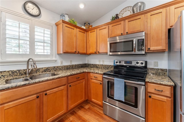 kitchen with dark stone counters, light wood-type flooring, appliances with stainless steel finishes, sink, and vaulted ceiling