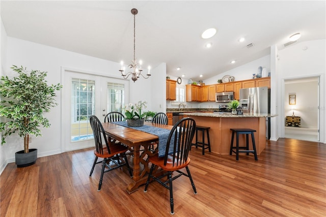 dining area with sink, light wood-type flooring, a chandelier, and vaulted ceiling