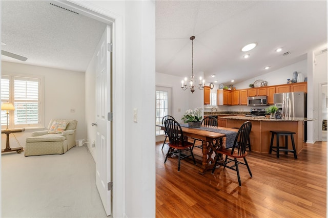 dining room featuring lofted ceiling, an inviting chandelier, a textured ceiling, hardwood / wood-style flooring, and sink