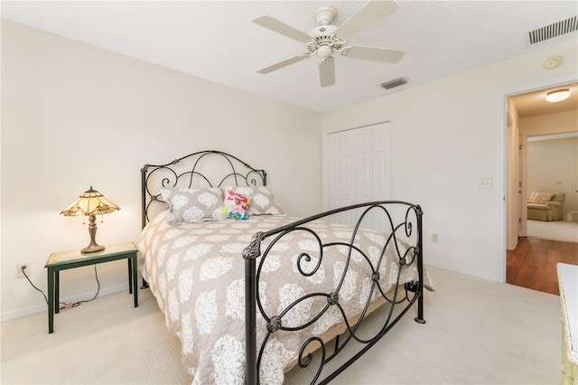 bedroom featuring a textured ceiling, light colored carpet, ceiling fan, and a closet