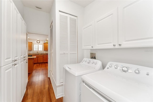 clothes washing area with cabinets, separate washer and dryer, sink, a textured ceiling, and light hardwood / wood-style flooring