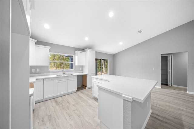 kitchen featuring vaulted ceiling, a kitchen island, sink, light hardwood / wood-style flooring, and white cabinetry