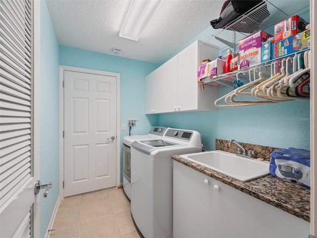 laundry area with cabinets, sink, washer and dryer, light tile patterned floors, and a textured ceiling