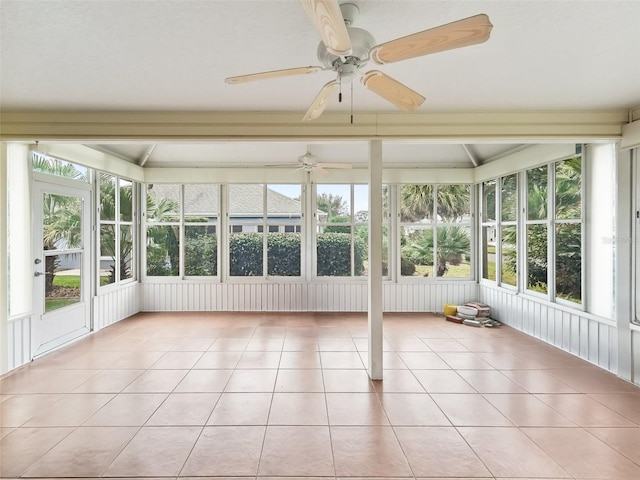 unfurnished sunroom featuring beamed ceiling, ceiling fan, and a healthy amount of sunlight