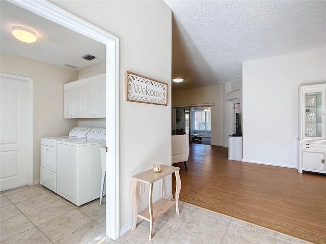 clothes washing area with a textured ceiling, light wood-type flooring, washing machine and dryer, and cabinets