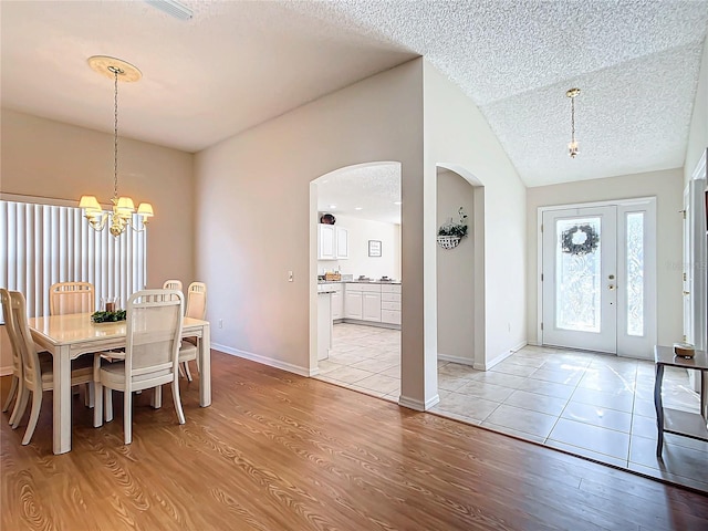 dining area featuring light hardwood / wood-style floors, lofted ceiling, a textured ceiling, and an inviting chandelier