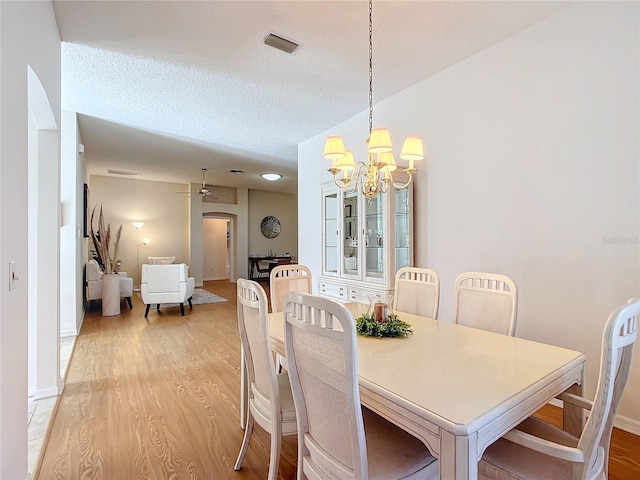 dining space with light wood-type flooring, ceiling fan with notable chandelier, and a textured ceiling