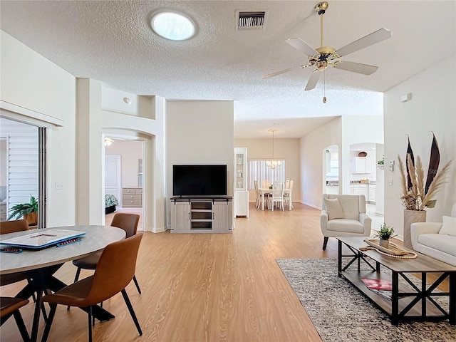 living room with a textured ceiling, light hardwood / wood-style floors, and ceiling fan with notable chandelier