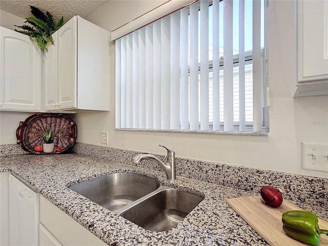 kitchen with white cabinetry, sink, a textured ceiling, and light stone counters