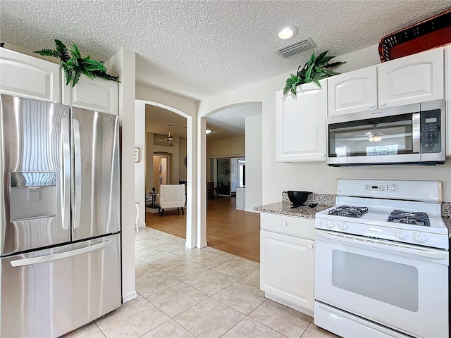 kitchen featuring stainless steel appliances, dark stone countertops, a textured ceiling, white cabinets, and light wood-type flooring