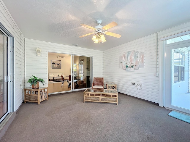 living area with dark colored carpet, wooden walls, and a textured ceiling