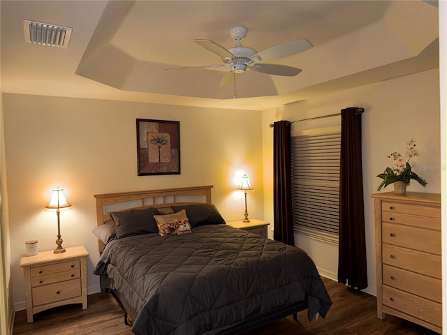 bedroom with dark wood-type flooring, ceiling fan, and a raised ceiling