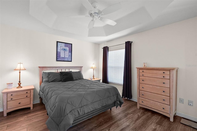 bedroom with ceiling fan, dark hardwood / wood-style flooring, and a raised ceiling