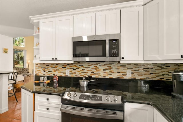 kitchen featuring tile patterned flooring, backsplash, dark stone countertops, white cabinets, and appliances with stainless steel finishes