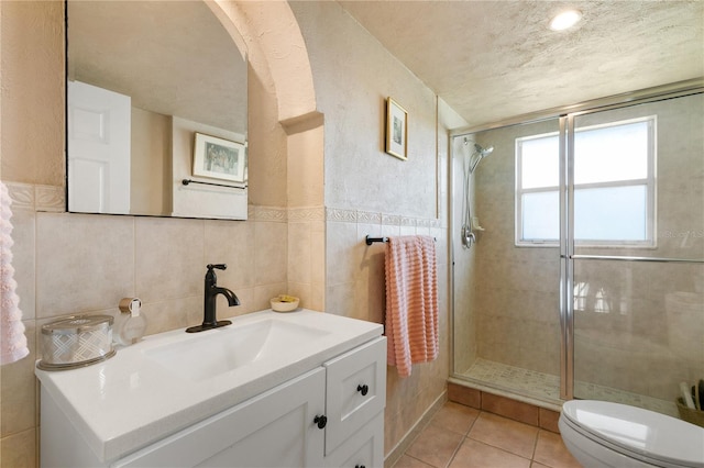 bathroom featuring tile patterned floors, vanity, tile walls, toilet, and a shower with shower door