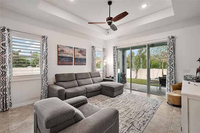 living room featuring light tile patterned floors, ceiling fan, and a raised ceiling