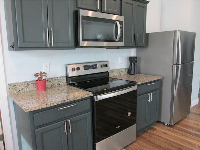 kitchen featuring gray cabinetry, dark hardwood / wood-style floors, light stone countertops, and stainless steel appliances