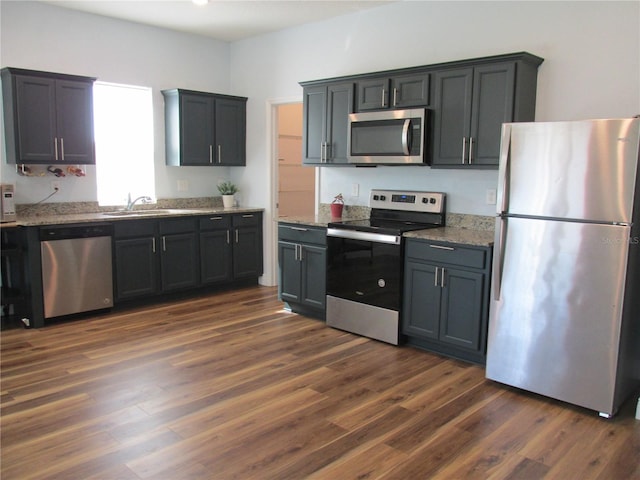 kitchen with light stone counters, dark hardwood / wood-style flooring, stainless steel appliances, and sink