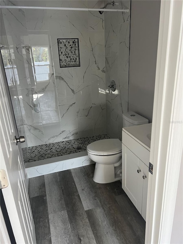 bathroom with hardwood / wood-style flooring, vanity, toilet, and tiled shower