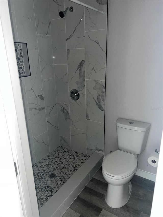 bathroom with toilet, wood-type flooring, and a tile shower