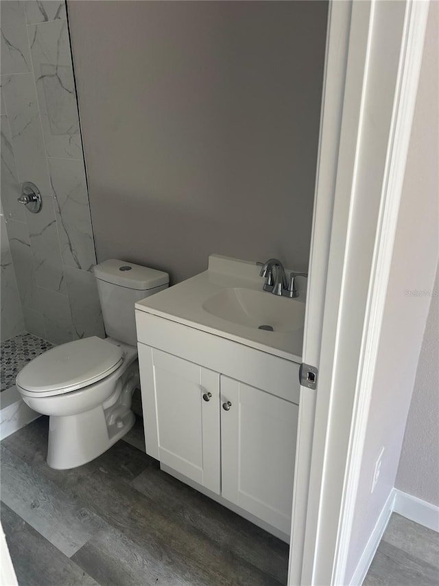 bathroom featuring a tile shower, vanity, toilet, and wood-type flooring