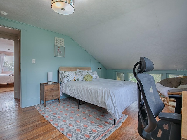 bedroom with light hardwood / wood-style floors, lofted ceiling, and a textured ceiling