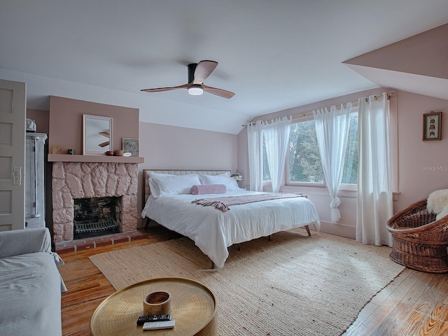 bedroom featuring a stone fireplace, light hardwood / wood-style floors, lofted ceiling, and ceiling fan