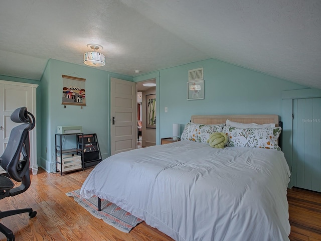 bedroom with wood-type flooring, a textured ceiling, and vaulted ceiling