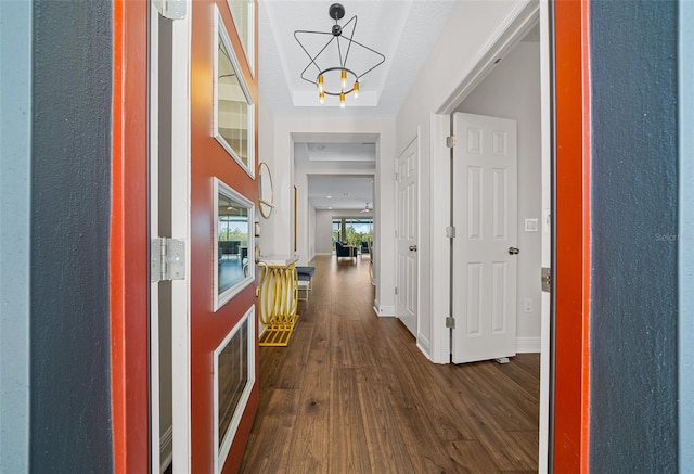 hallway featuring dark hardwood / wood-style floors, a raised ceiling, and a chandelier