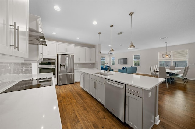 kitchen featuring sink, hanging light fixtures, stainless steel appliances, extractor fan, and a center island with sink