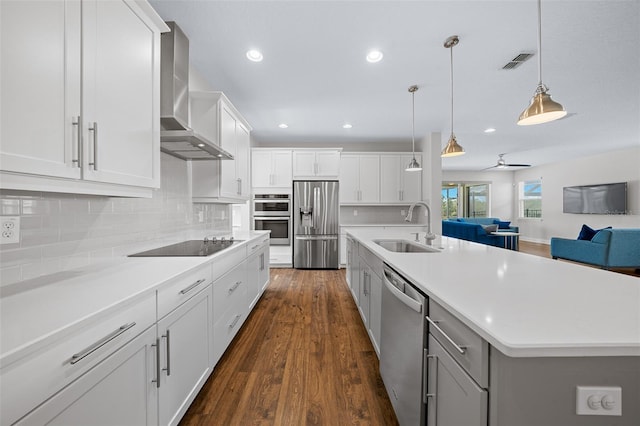 kitchen featuring sink, wall chimney exhaust hood, hanging light fixtures, stainless steel appliances, and a spacious island