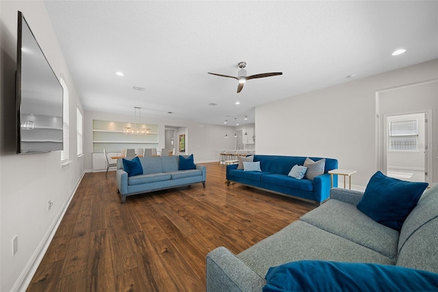 living room featuring ceiling fan with notable chandelier, wood-type flooring, and built in shelves