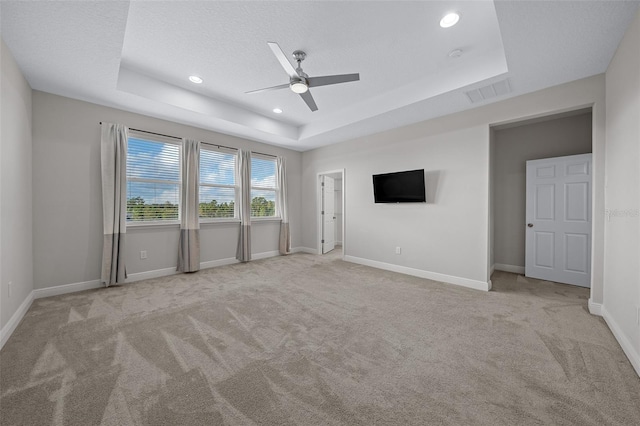 unfurnished bedroom with ceiling fan, a raised ceiling, light colored carpet, and a textured ceiling