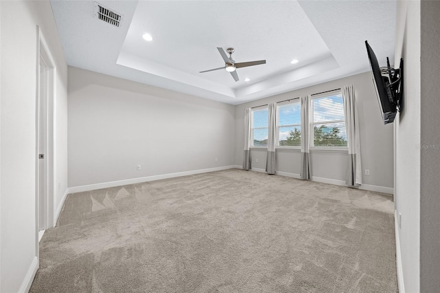 empty room with light carpet, a tray ceiling, and ceiling fan