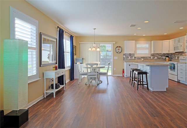 kitchen featuring white cabinetry, pendant lighting, dark wood-type flooring, white appliances, and a center island