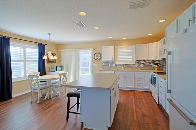 kitchen with dark wood-type flooring, a kitchen island, white appliances, and white cabinets