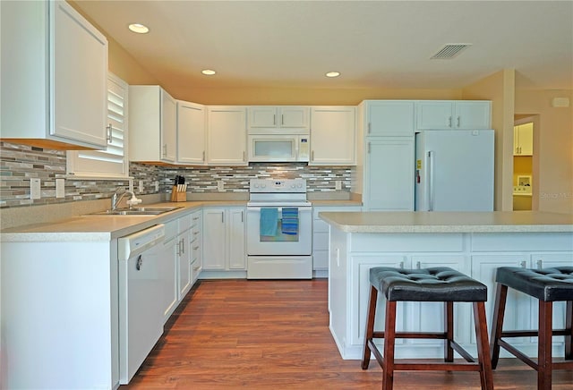 kitchen with dark wood-type flooring, white cabinets, sink, a breakfast bar, and white appliances