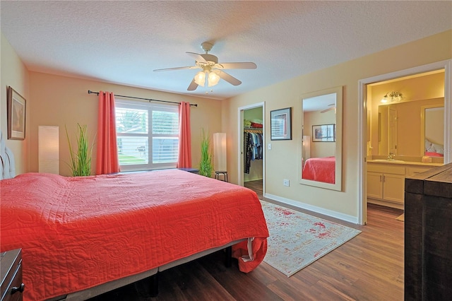 bedroom with a walk in closet, a textured ceiling, hardwood / wood-style flooring, ceiling fan, and ensuite bathroom