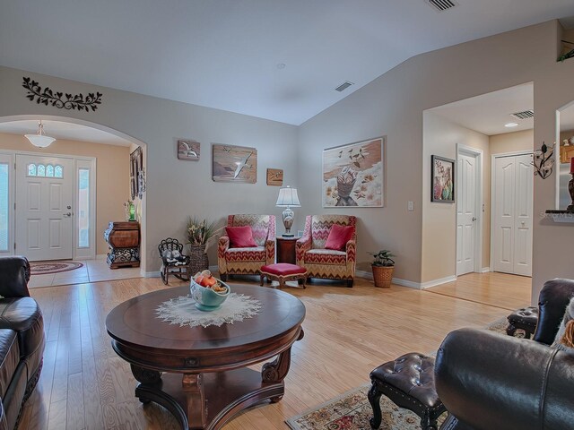 living area with vaulted ceiling, light wood-style floors, arched walkways, and baseboards