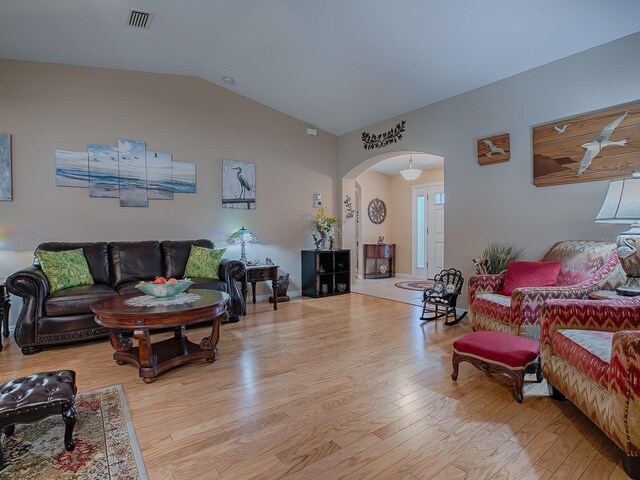 living area with arched walkways, wood finished floors, and lofted ceiling